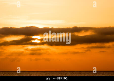 Il sorgere del sole sopra il canale inglese. Sun sopra l'orizzonte parzialmente nascosti dallo strato di nubi. Orange sky. Visto da di Ramsgate nel Kent. Foto Stock