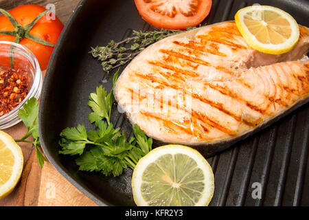 Filetto di salmone alla griglia sulla padella. Bistecca di salmone guarnire limone sul nero ardesia. Sfondo di legno. Delisious sano concetto di cibo. Vista dall'alto. Visualizza f Foto Stock