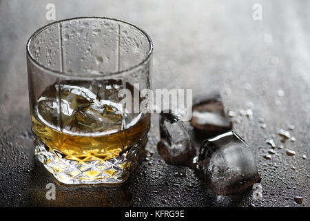 Whisky in un bicchiere e pezzi di ghiaccio su un legno Foto Stock