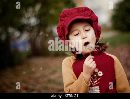 Bella ragazza che soffia un dente di leone nel parco. Scena autunnale, atmosfera retrò Foto Stock