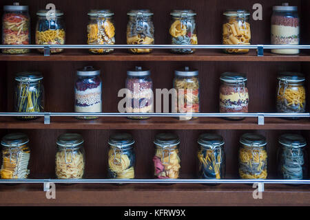 Sui ripiani in legno sono vasi di vetro con varicolored vari tipi di pasta, spaghetti, fagioli, cereali per il loro stoccaggio e decorare la cucina Foto Stock