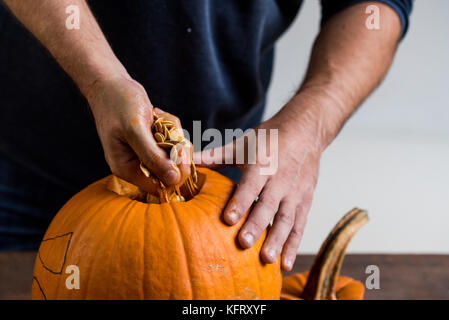 Mani maschio carving zucca tenendo fuori i semi Foto Stock