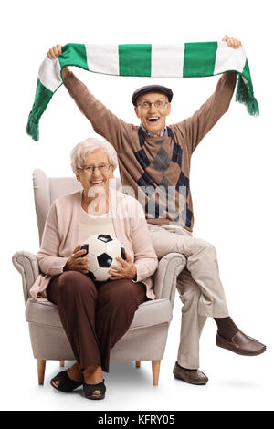 Overjoyed anziani appassionati di calcio con un campo di calcio e un foulard seduto in poltrona e rasserenanti isolati su sfondo bianco Foto Stock