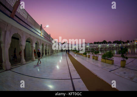 Delhi, India - 19 settembre 2017: unidentified gente camminare nei pressi del laghetto artificail, con una bella vista del famoso Gurdwara Sikh tempio dorato Harmandir Sahib si riflette nel laghetto artificiale, con uno splendido cielo viola in India Foto Stock