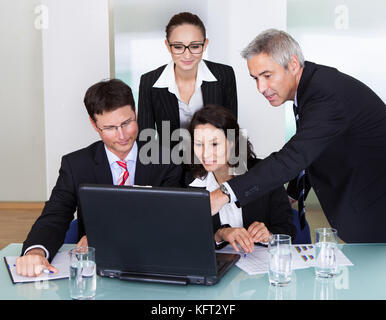 Quattro diversi operatori professionali aventi una discussione e una sessione di brainstorming riuniti attorno a un computer portatile Foto Stock