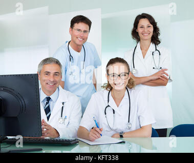 Il team medico comprendente maschio e femmina che pongono i medici insieme sorridente in ufficio con la videocamera Foto Stock