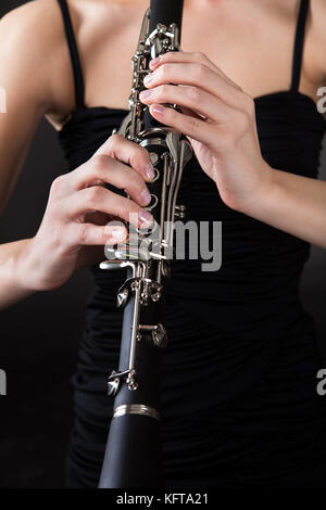 Bella giovane donna giocando clarinetto su sfondo nero Foto Stock