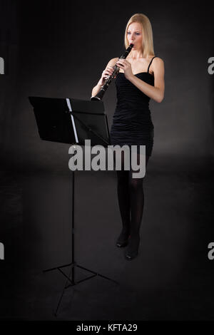 Bella giovane donna giocando clarinetto su sfondo nero Foto Stock