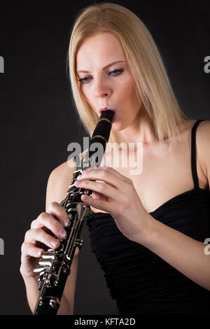 Bella giovane donna giocando clarinetto su sfondo nero Foto Stock