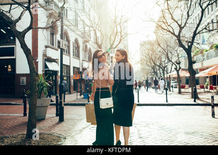 Felice di giovani donne con le borse della spesa a piedi lungo la strada della citta'. Vista posteriore del colpo di amici di sesso femminile per lo shopping in città. Foto Stock