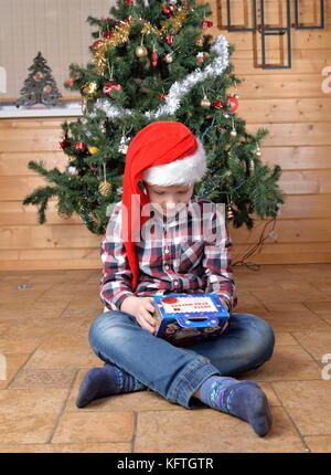 Il ragazzo si siede sul pavimento e ritiene che il dono di un albero di natale. Foto Stock