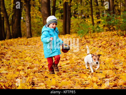 Little Boy passeggiate piacevolmente il suo cane al guinzaglio in un bel parco di caduta Foto Stock