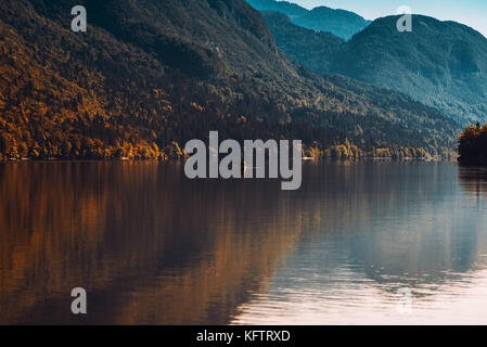 Uomo in barca a remi sul lago di Bohinj in Slovenia. autunno magnifico paesaggio con il lago glaciale di superficie d'acqua e montagne che la circondano. Foto Stock