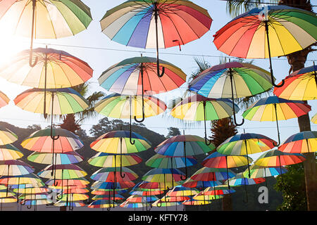 Ombrelloni colorati sfondo. Multi-ombrelloni colorati nel cielo galleggiante sopra la strada contro gli alberi di palma. Ombrello street decorazione. Ombrellone Foto Stock