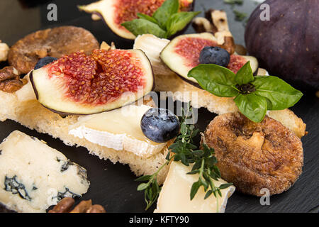 Sovraccarico di fichi, fichi secchi, snack sandviches con brie, blue cheese fig fette, pinoli e mirtillo nero su sfondo di ardesia. Vista dall'alto. Dietin Foto Stock