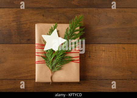 Regalo di natale presente avvolto in riciclata carta di avvolgimento con naturale evergreen decorazioni e un vuoto, a forma di stella tag regalo su uno sfondo di legno Foto Stock