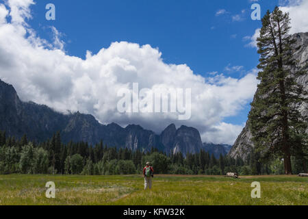 Vista orizzontale, sul retro di un uomo maschio escursionista guardando a Mountain View da un prato in Yosemite National Park, California USA Foto Stock