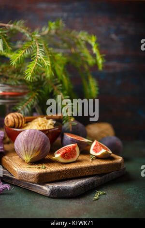 Succosa fresco intero di fig frutti e un taglio di fichi e ciotola di miele in favi sul tagliere di legno su sfondo verde scuro Foto Stock