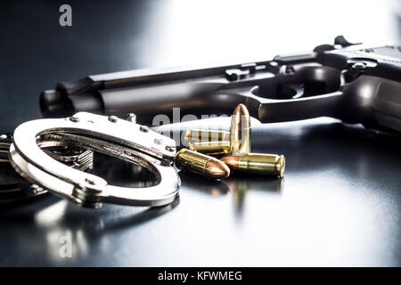 Pistola proiettili, pistola e manette su tavola nera. Foto Stock