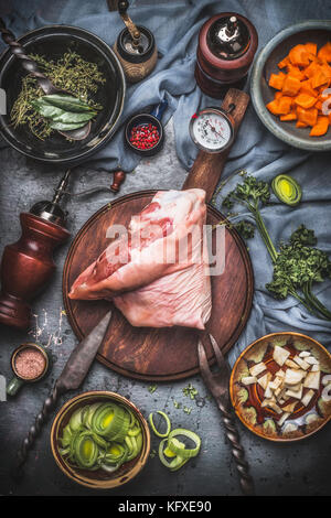 Carne di maiale cruda eisbein fuso a snodo , angolo cottura per la preparazione di arrosti con verdure gut in ciotole con carne di rustico coltello e forchetta sul tagliere, vista dall'alto. coun Foto Stock