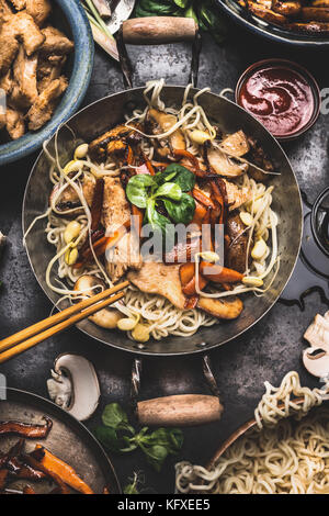 Piatto asiatico con pollo verdure noodle soffriggere in poco wok con baguette e cottura ingredienti, vista dall'alto Foto Stock