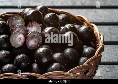 Jabuticabas, noto anche come il brasiliano berry o grapetree brasiliano (plinia cauliflora) frutti su un vitigno di legno cestello, nero con un background in legno Foto Stock