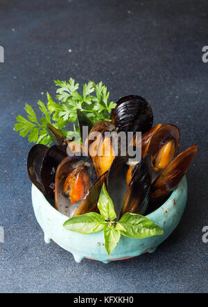 Cozze al forno con il burro ed il prezzemolo in ceramica blu ciotola e tazza di salsa su sfondo scuro dello sfondo. Spazio di copia Foto Stock