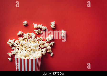 Scatola a strisce con popcorn su sfondo rosso Foto Stock