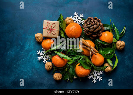 Luminose tangerini foglie verdi pigne confezione regalo fiocchi di neve ornamenti su sfondo blu scuro. natale anno nuovo biglietto di auguri composizione. banner Foto Stock