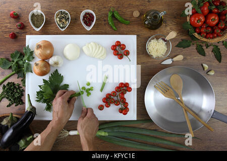 Alimentari top view, mani il taglio di sedano bianco sul tagliere in cucina topwork in legno con pomodori, verdura e pentola Foto Stock