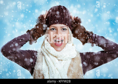 Giovane ragazza vivace in abbigliamento invernale con le mani sul suo capo, rallegrandosi per la prima neve. Foto Stock