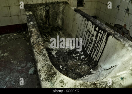 Una vecchia vasca all'interno un abbandonato ospedale psichiatrico, molto sporco e incrostato Foto Stock