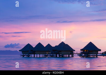 Una Rosa tramonto si riflette nell'acqua sotto elevata bungalows in intercontinental le moana resort bora bora, Polinesia francese. Foto Stock