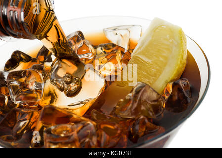 Versando cola in vetro con cubetti di ghiaccio e la fetta di limone, su sfondo bianco Foto Stock