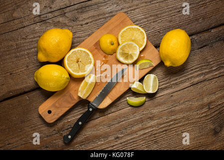 I limoni, coltello e le fette di limone sul tagliere, su un tavolo di legno. Foto Stock