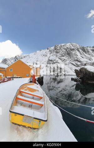 Fibra di vetro gialla canotto di pesca a terra sul snowcovered gangplank-n.molo laterale nusfjord del villaggio di pescatori porto-arancione pesca stagionale capanne o rorbu Foto Stock
