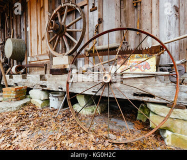 Vecchia ruota in ferro scartata e ruota in legno dietro la vecchia cabina in legno nella campagna dell'Alabama, USA. Foto Stock