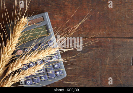 Spighe di grano e calcolatrice giacente su una superficie di legno con spazio di copia Foto Stock