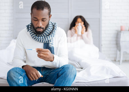Sconvolto uomo malato guardando il termometro Foto Stock