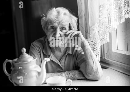 Ritratto di una donna anziana in una tabella con una pentola di tè. in bianco e nero photo. Foto Stock
