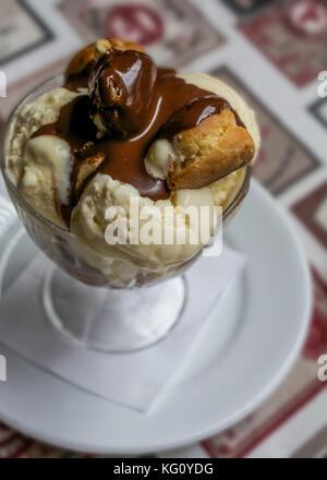 Profiterole alla vaniglia ricoperto di cioccolato fuso sulla piastra bianca su un tavolo Foto Stock