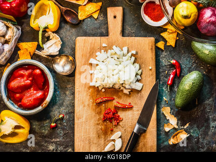 Spezie tritate sul tagliere di legno con coltello: peperoncino, cipolla e aglio con verdure ingredienti per cucina messicana on dark cucina rustica tab Foto Stock