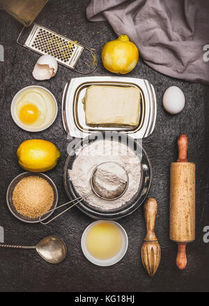 Cuocere gli ingredienti e gli strumenti per il limone cookie o torta rendendo la pasta su sfondo scuro, vista dall'alto, laici piatta Foto Stock