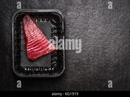 Tonno crudo filetto di pesce in scatola di plastica nero su sfondo rustico, vista dall'alto, luogo di testo. sano concetto di frutti di mare Foto Stock