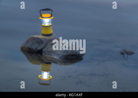 Vista notturna di luminosa lanterna a mano in piedi sulla roccia nel lago Foto Stock