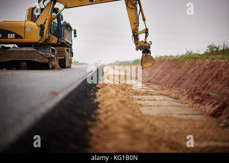 La costruzione di strade, asfalto per pavimentazione stradale, tempra, escavatore lavorando su strada in costruzione Foto Stock