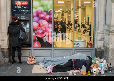 Londra, Regno Unito. 2° Nov, 2017. Traversine ruvida dormire con i loro beni al di fuori di un supermercato Tesco nella città di Londra. Gli amanti dello shopping andare circa la loro attività all'interno e una signora raccoglie denaro dalla macchina accanto a loro. Credito: Guy Bell/Alamy Live News Foto Stock