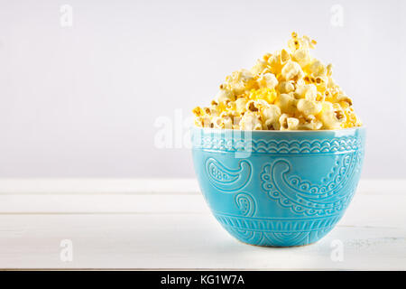 Popcorn salato in una tazza di colore blu è su un tavolo di legno Foto Stock