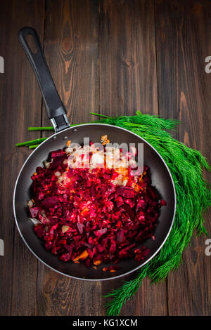 Carote, barbabietole e cipolle in una padella, intorno all aneto, su di un legno marrone background. Ingredienti per borsch Foto Stock