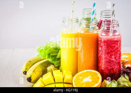 Diversi i frullati in bottiglie di mango, arancio, banana, sedano, bacche, su di un tavolo di legno Foto Stock